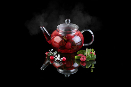 Glass teapot with black tea. Mint, cranberry, raspberry. On a black background with reflectionの写真素材