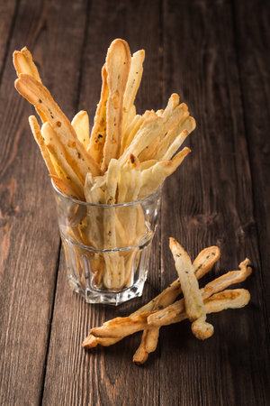 Grissini bread sticks in a glass cup on a wooden brown background.