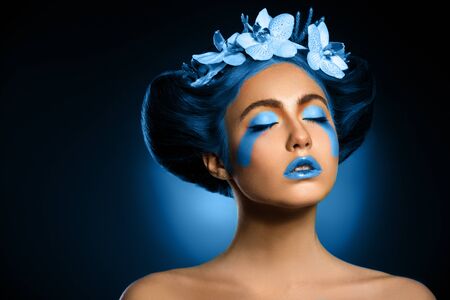 Portrait of a beautiful woman with blue makeup and orchd in hair, toned in color of the year 2020, classic blue.の写真素材