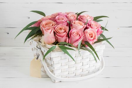 White basket with beautiful pink roses, on a white wooden background.の写真素材