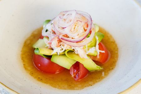 Fresh salad with king crab meat and avocado in a plate. Served with sauce and fresh tomatoes.