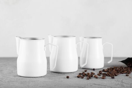 Three white milk jugs on a gray decorative background. Coffee beans are scattered nearby.の写真素材