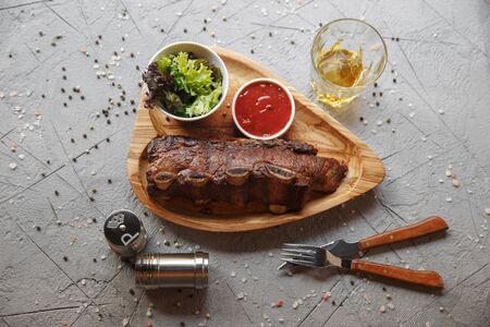Grilled pork ribs served on a wooden board with salad and sauce.の写真素材