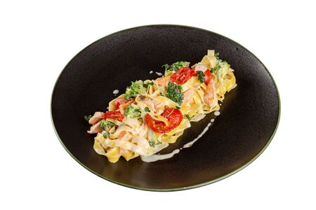 Fettuccine pasta with salmon, cream sauce, tomatoes and parmesan. On a black plate, isolated on a white background.の写真素材