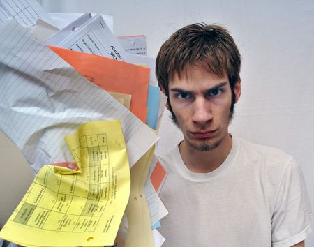 Angry young man ripping holding up an overload of paperwork. Slightly tinted with a blue tone intentionally to add dramatic effect. Nothing copyrighting is contained in the papersの写真素材