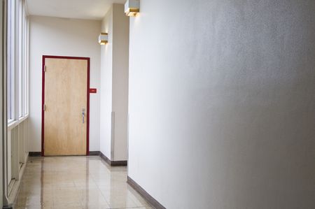 An empty hallway leading to a closed door. Windows let light into the hall coming from the left.の写真素材