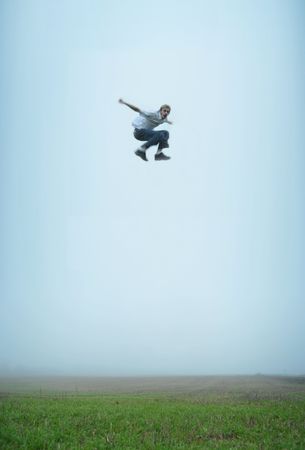 A man makes a massive jump in an empty field. He is flying in mid air!の写真素材