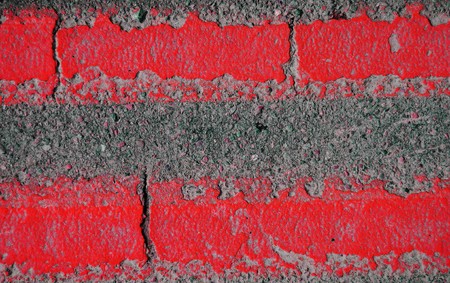 An old background closeup texture of a double red line on an asphalt street roadの写真素材