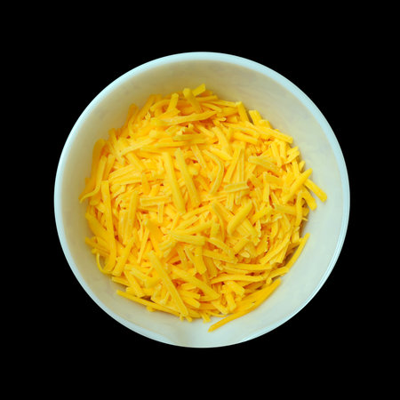 An aerial view of a white bowl containing yellow cheddar cheese isolated on a pitch black background. の写真素材