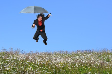 Young businessman jumping over a grass field with blank blue sky copyspace.の写真素材