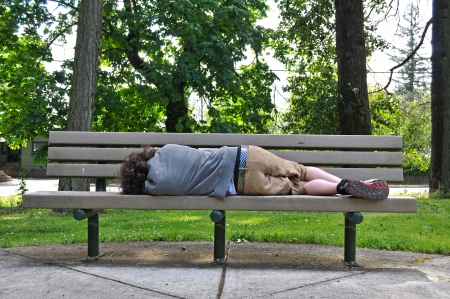 A homeless person takes a nap on a bench in a public park.の写真素材