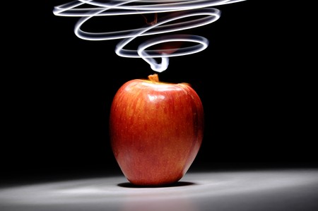 An apple sitting on a white surface with light painting streaks above and around the apple.の写真素材