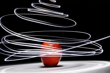 An apple sitting on a white surface with light painting streaks above and around the apple.の写真素材