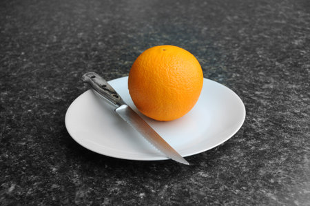 An orange fruit on a white plate with a knife