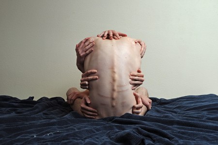 Man sitting on a bed grabbing his back in all different kinds of ways.の写真素材