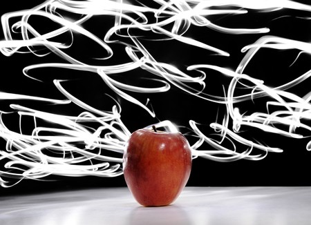 An apple sitting on a white surface with light painting streaks above and around the apple.の写真素材
