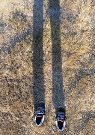 Choes casting a shadow of an invisible man's legs on grassの写真素材