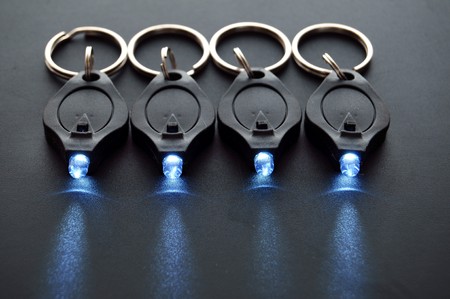 Miniature LED keychain lights on a black surface with shallow depth of field.の写真素材
