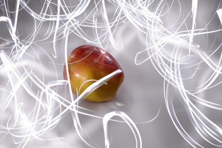 An apple sitting on a white surface with light painting streaks above and around the apple.の写真素材