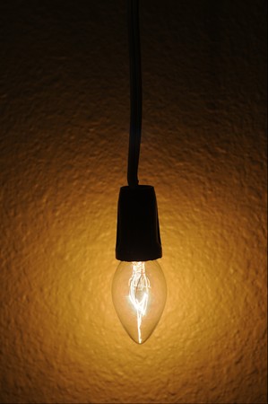 A small clear light bulb hanging next to a wallの写真素材
