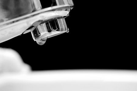 A silver and shiny tap water sink faucet with a barely noticeable drop of water dripping out of the faucet. Lots of copyspace below with room for text.の写真素材