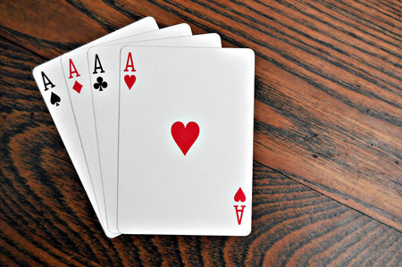 A group of four playing card aces on a stained oak wooden table.