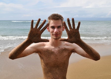 Beach fun with a young attractive male with sand all over his body. Ocean sandy beach waves in the background.の写真素材