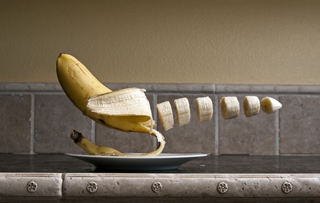 Banana floating over a plate chopped up over a kitchen counter top.の写真素材