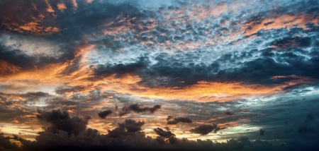 Blue sky with orange sunlit clouds coming from behind the clouds.の写真素材