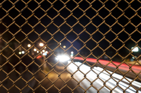 fence at night with traffic on the freeway at night time