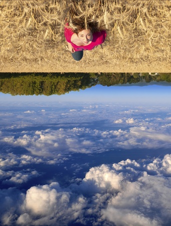 Attractive young teenage white Caucasian female floating above a beautiful field landscape with upside down clouds の写真素材