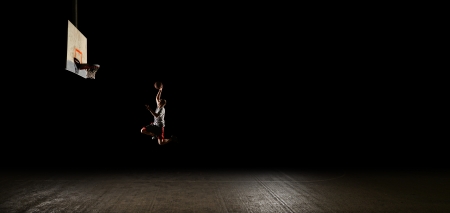 Basketball court at night with lights on, basketball player jumping and aiming at hoopの写真素材