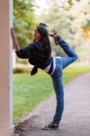 Young girl is stretching her leg, while holding on to a wallの写真素材