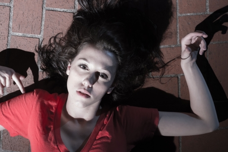 Image of a young female model wearing pretty red top lying on the floor of bricks.の写真素材