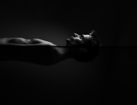 Image of a man floating inside of a sensory deprivation isolation tank, also known as a salt water floatation tank, a tank used in meditation, therapy and alternative medicine. This image has darker water.の写真素材