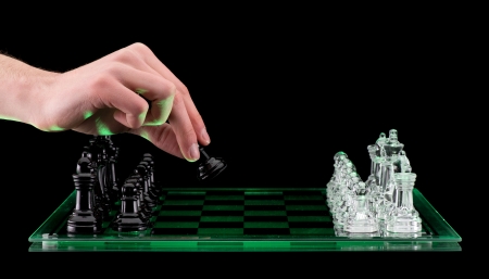 A hand makes the first move picking up a Glass pawn chess pieces on a glass chessboard with a reflection isolated on a black backgroundの写真素材