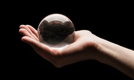 Hand holding a clear transparent crystal glass ball in their palm isolated on black backgroundの写真素材