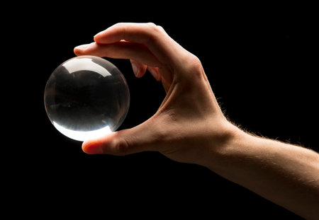 Hand holding a clear transparent crystal glass ball isolated on black background