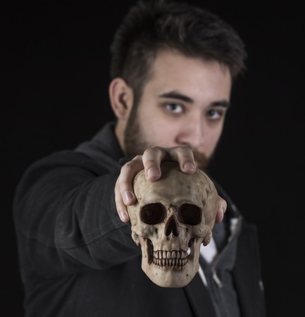 Gorgeous Young Man Wearing Black Jacket Shirt Holding Skull While Looking at the Camera. Isolated on Black Background.の写真素材