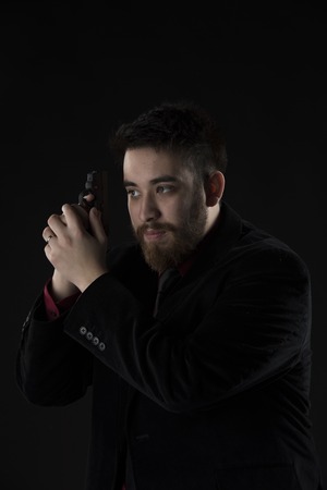 Half Body Shot of Gorgeous Goatee Man Wearing Black Suit Holding Small Black Gun. Isolated on Black Background.の写真素材