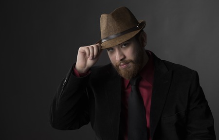 Close up Gorgeous Young Man in Business Suit Holding his Brown Hat While Looking at the Camera. Isolated on Gray Background.の写真素材