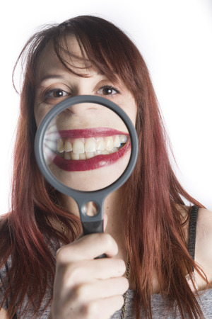 Playful Young Teenage Woman Holding Magnifying Glass in front of Mouth to Enlarge Toothy Smileの写真素材