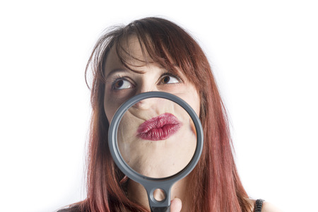 Perplexed Looking Young Woman with Magnifying Glass in front of Puckered Up Mouth Looking as if Thinking Hardの写真素材