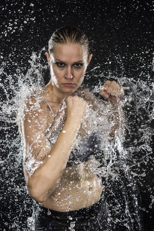 Half Body Shot of a Athletic Female Fighter in Water Splashes Looking Fierce at the Camera Against Black Background.の写真素材