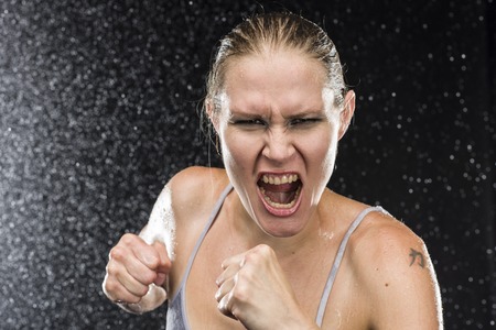 Close up Female Fighter Shouting Out Loud at the Camera with Angry Facial Expression Against Black Background with Water Drops Effect.の写真素材