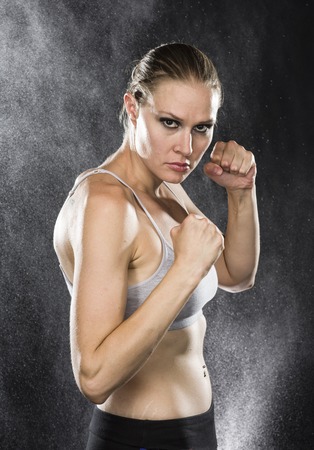half Body Shot of an Athletic Woman in Combat Pose Looking Fierce at the Camera Against Water Drops Background.の写真素材