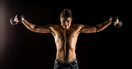 Man stretching arms outward doing a Standing Dumbbell Chest Fly. Studio composite over black.の写真素材