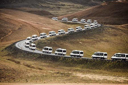 Tour bus vans on a curved road leading through a mountain landscape in Iceland.の写真素材