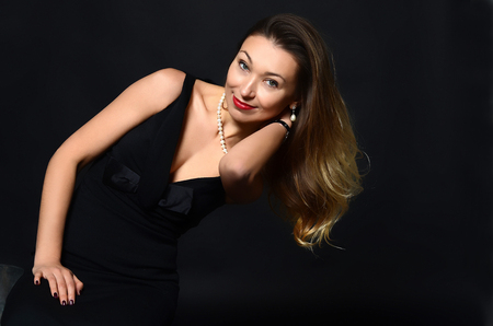 White woman with long brown and blond hair in white pearl jewelry in long black evening dress on dark backgroundの写真素材