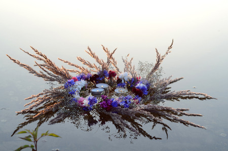 Wreath of flowers with burning candles on the waterの写真素材